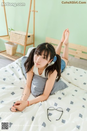 A woman sitting on top of a bed with her hand on her chin.