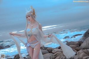 A woman in a blue bikini standing on a rocky beach.