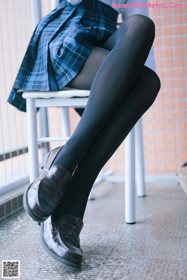 A woman sitting on a chair wearing black tights and a plaid skirt.