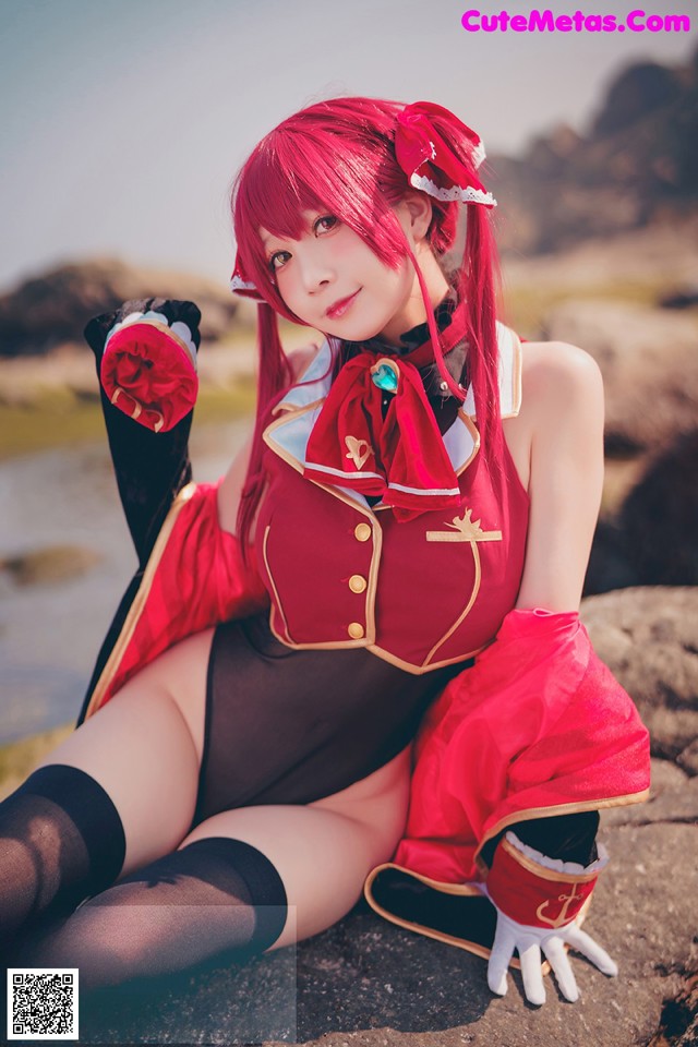 A woman in a red and black outfit sitting on a rock.