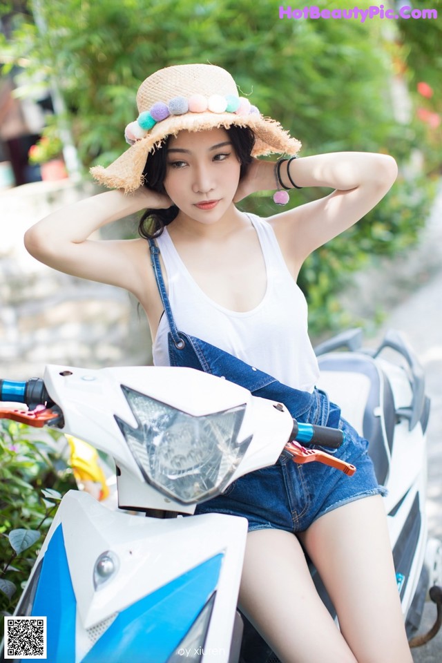 A woman sitting on a motorcycle wearing a straw hat.