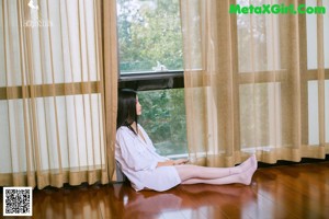 A woman in a white dress leaning against a window.