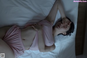 A woman in a pink top and shorts sitting on a bed.