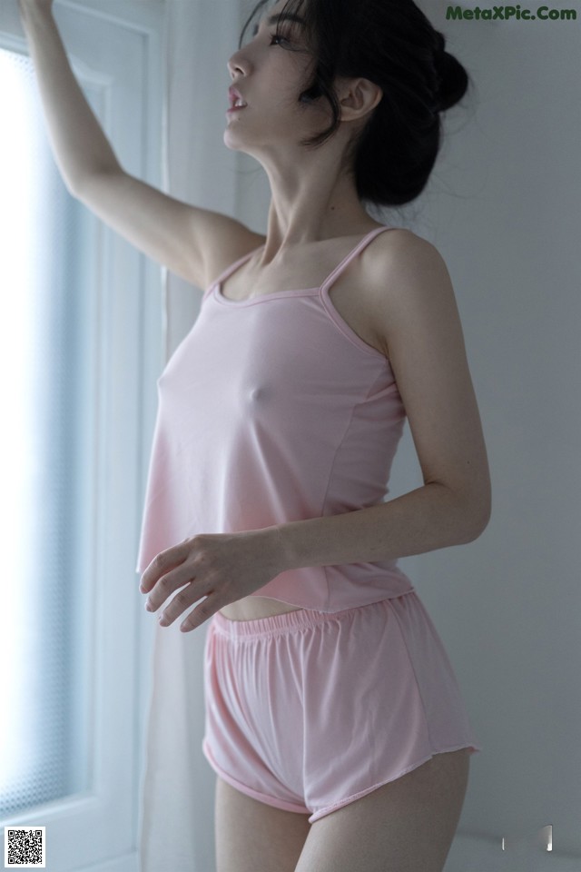 A woman in a pink tank top and shorts leaning against a window.