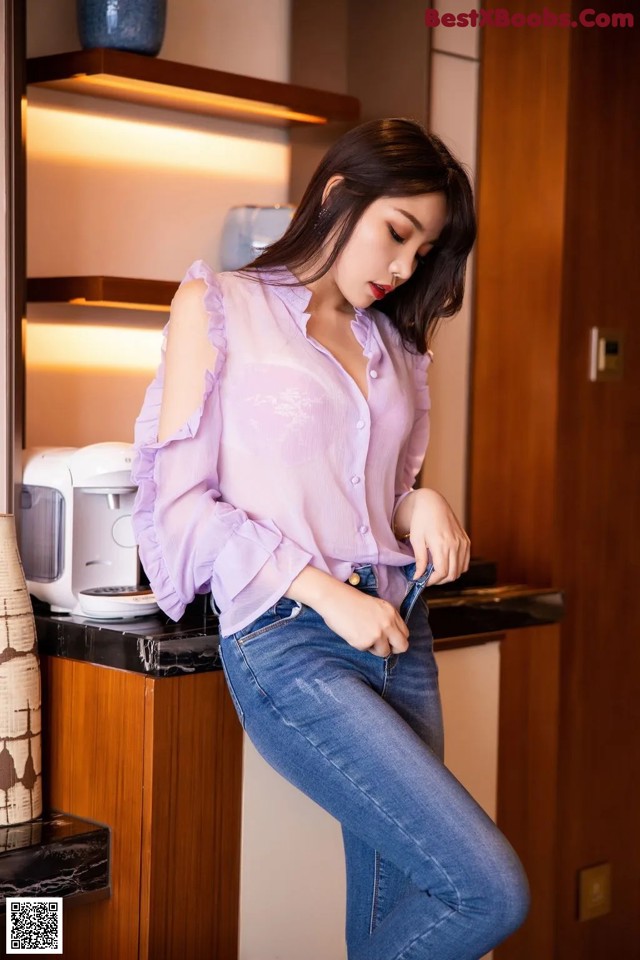 A woman in a pink shirt and jeans standing in a kitchen.