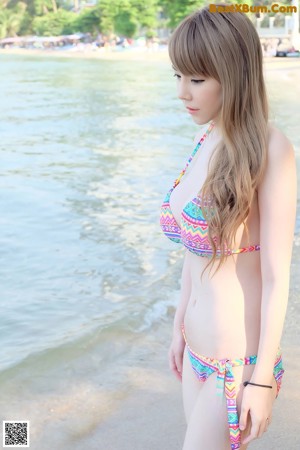A woman in a bikini crouching down on the beach.