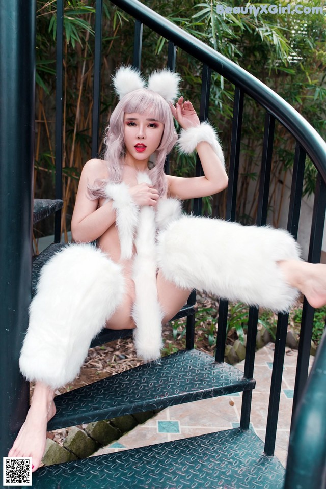 A woman in a white fur coat sitting on a set of stairs.