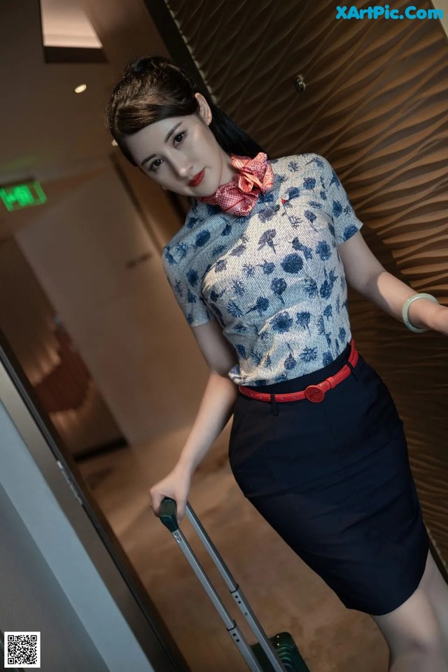 A woman in a blue shirt and black skirt with a red belt.