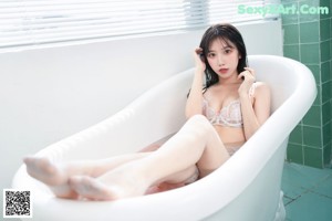 A woman sitting in a bathtub with her legs in the water.