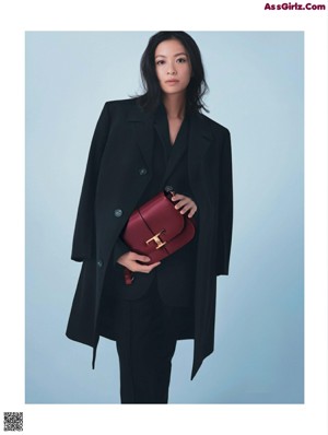 A woman in a black coat and black boots posing for a magazine.