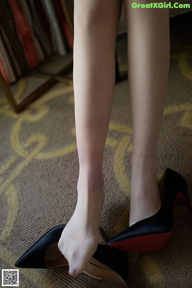 A close up of a woman's legs wearing black and red shoes.