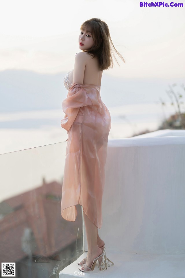 A woman in a pink dress standing on a balcony.