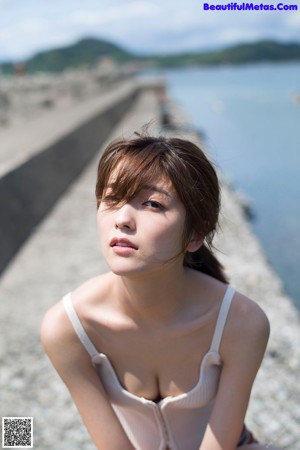 A woman in a white tank top and blue shorts leaning against a wall.