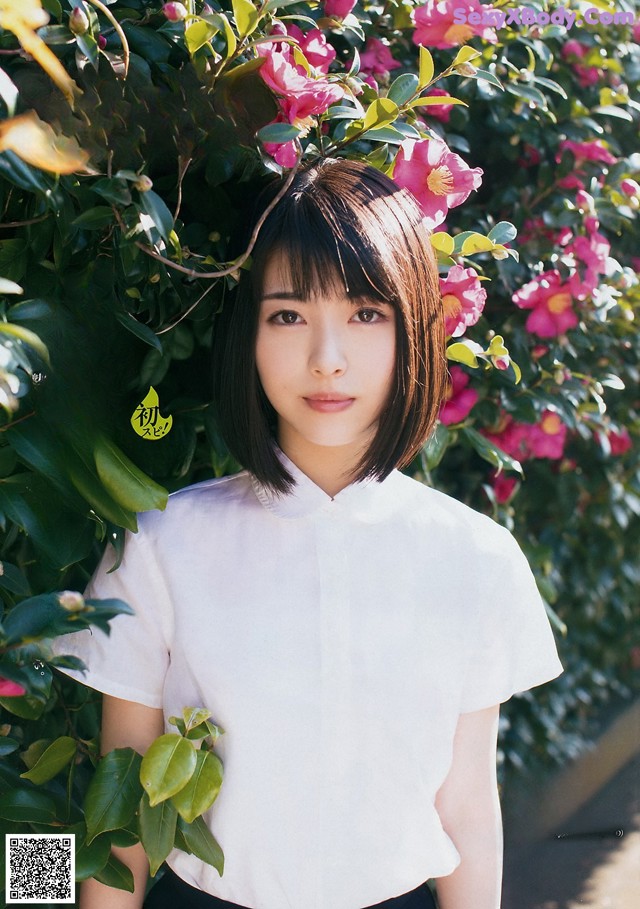 A woman standing in front of a bush of flowers.