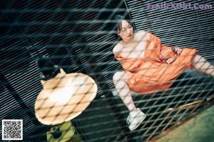 A woman in an orange jumpsuit sitting on the ground next to a tool box.