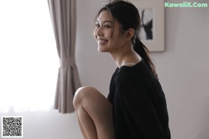 A woman in a black bra and panties sitting on a bed.